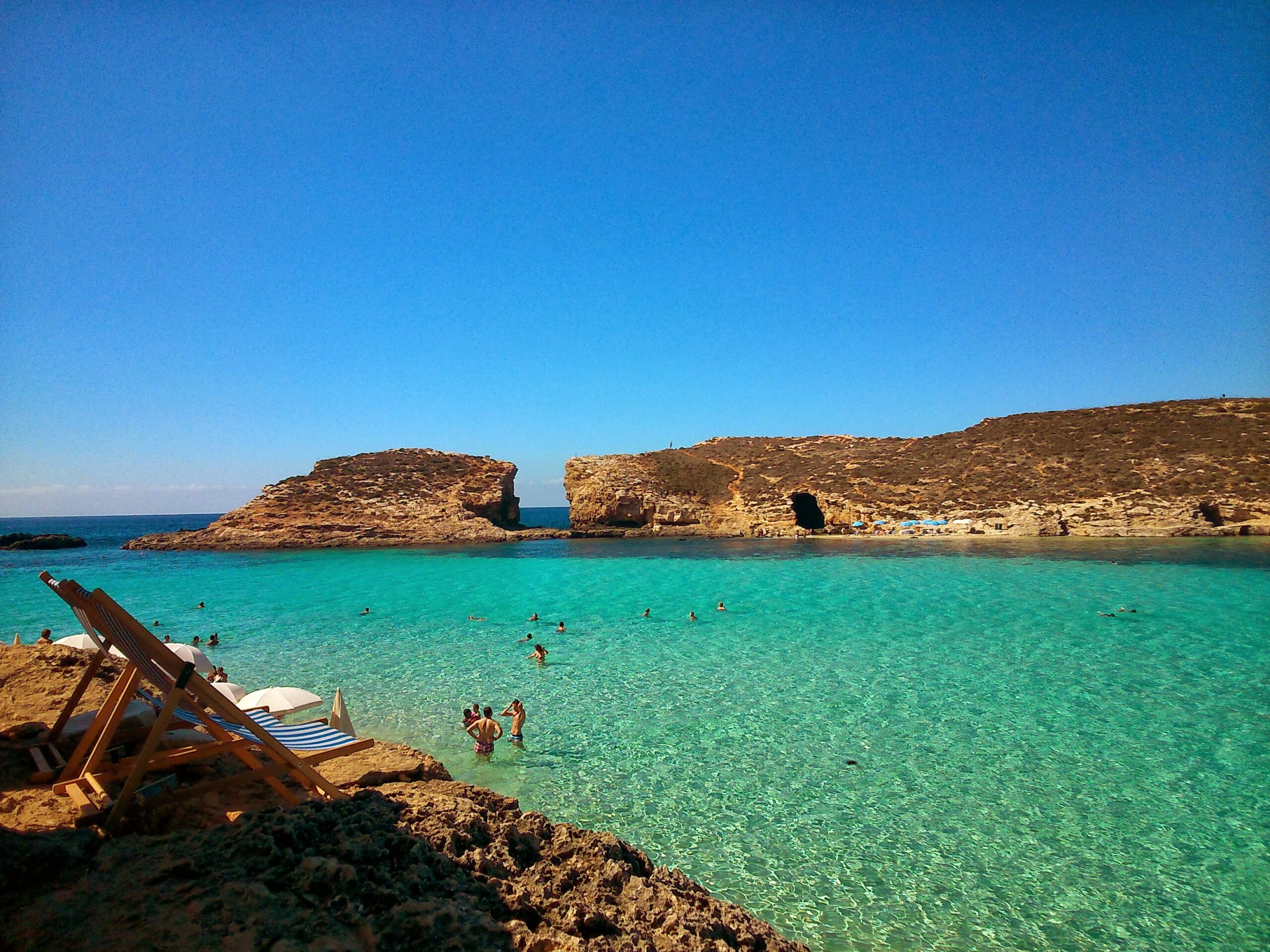 Turquoise lagoon with rocky headlands, swimmers and deckchairs on the shore