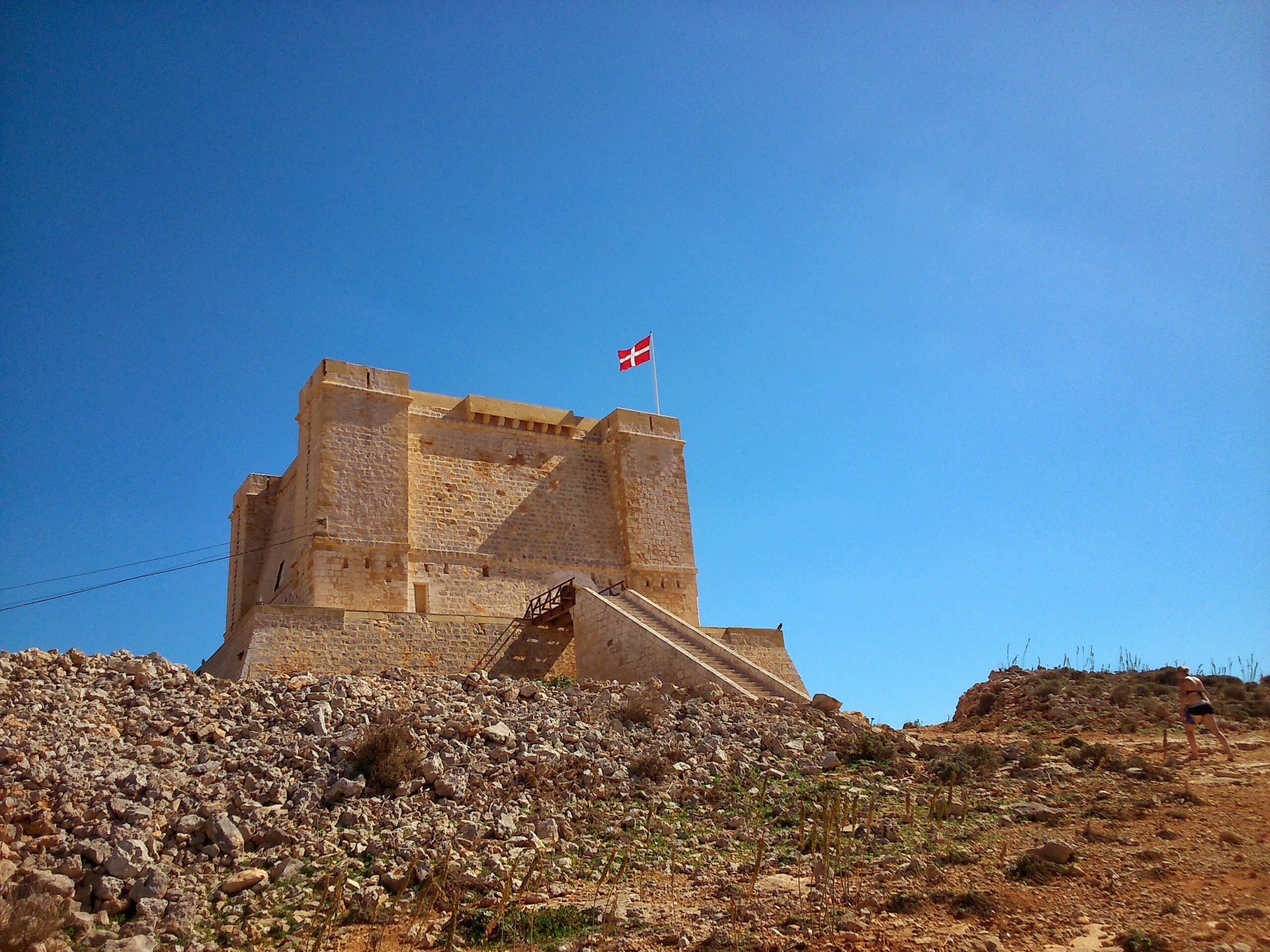 Sandstone fortress on a rocky hilltop with a flag flying against blue sky