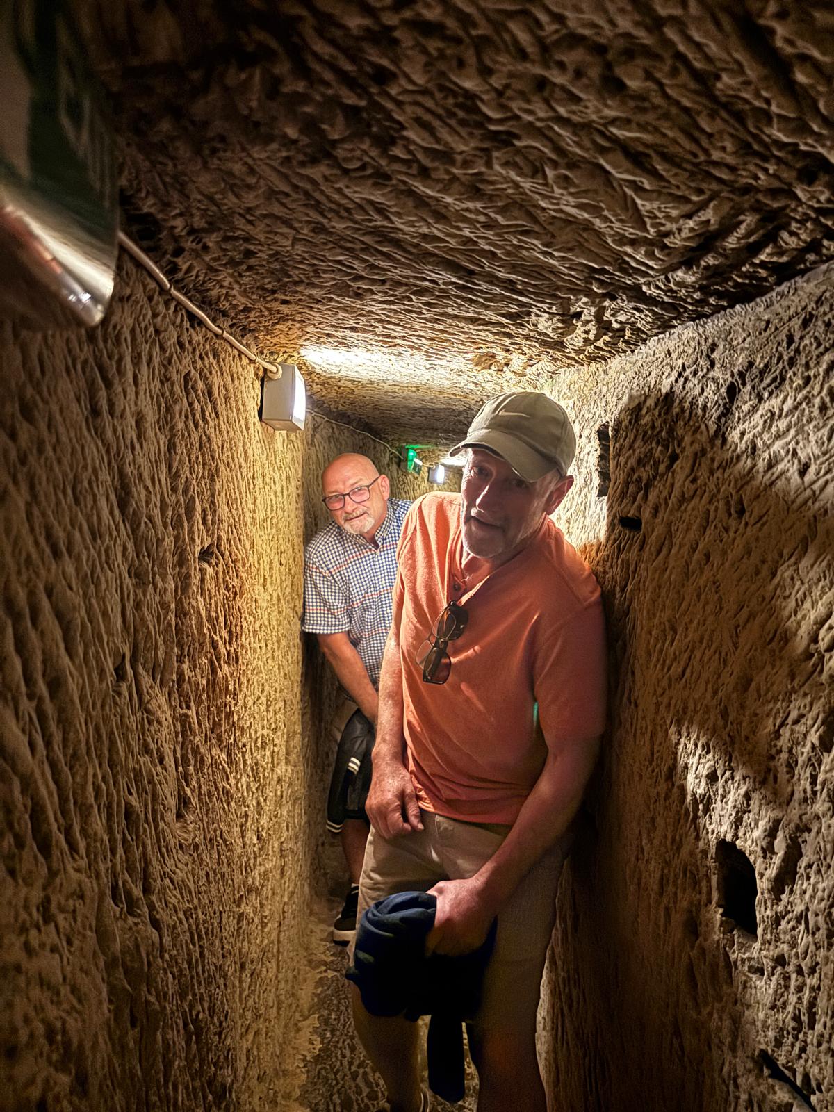 Two men walking through a narrow rock-cut tunnel passage