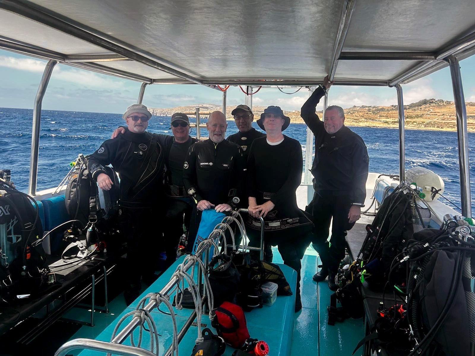 Group of divers in drysuits posing on a dive boat deck