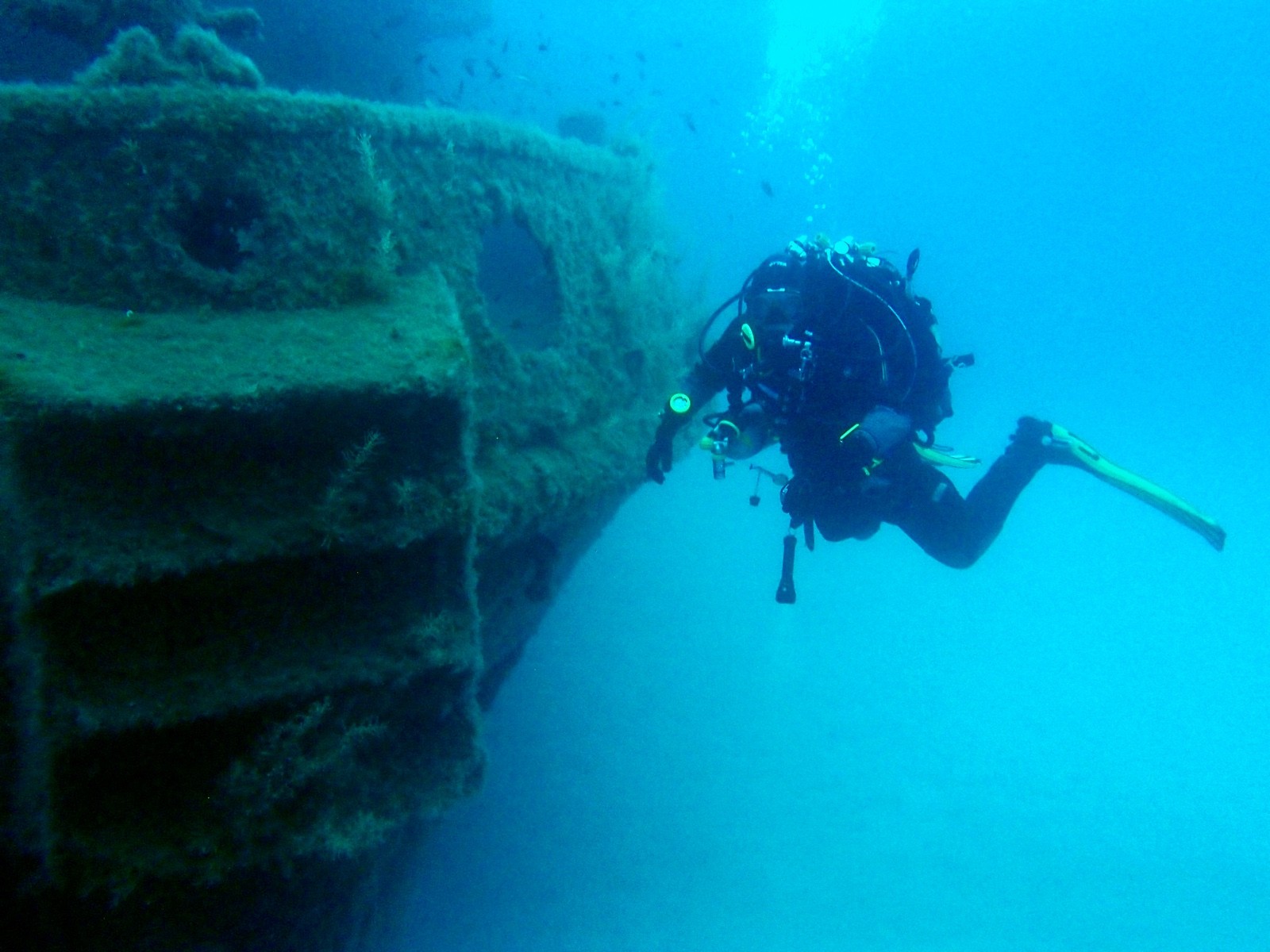 Tec diver next to the encrusted stern of a shipwreck in clear blue water