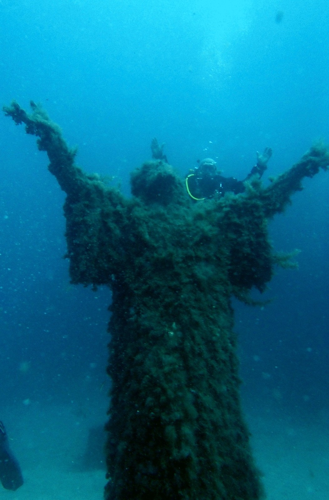 Diver behind a large algae-covered underwater statue with raised arms