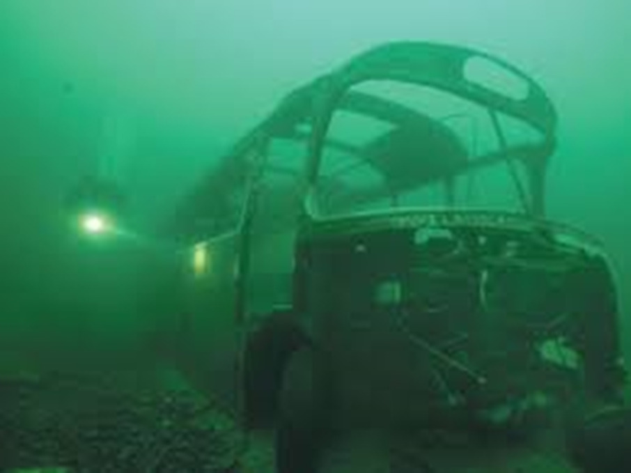 Sunken bus wreck underwater with a diver's torch beam in the distance
